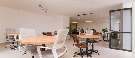 A modern conference room with round tables and white chairs, equipped with individual monitors.