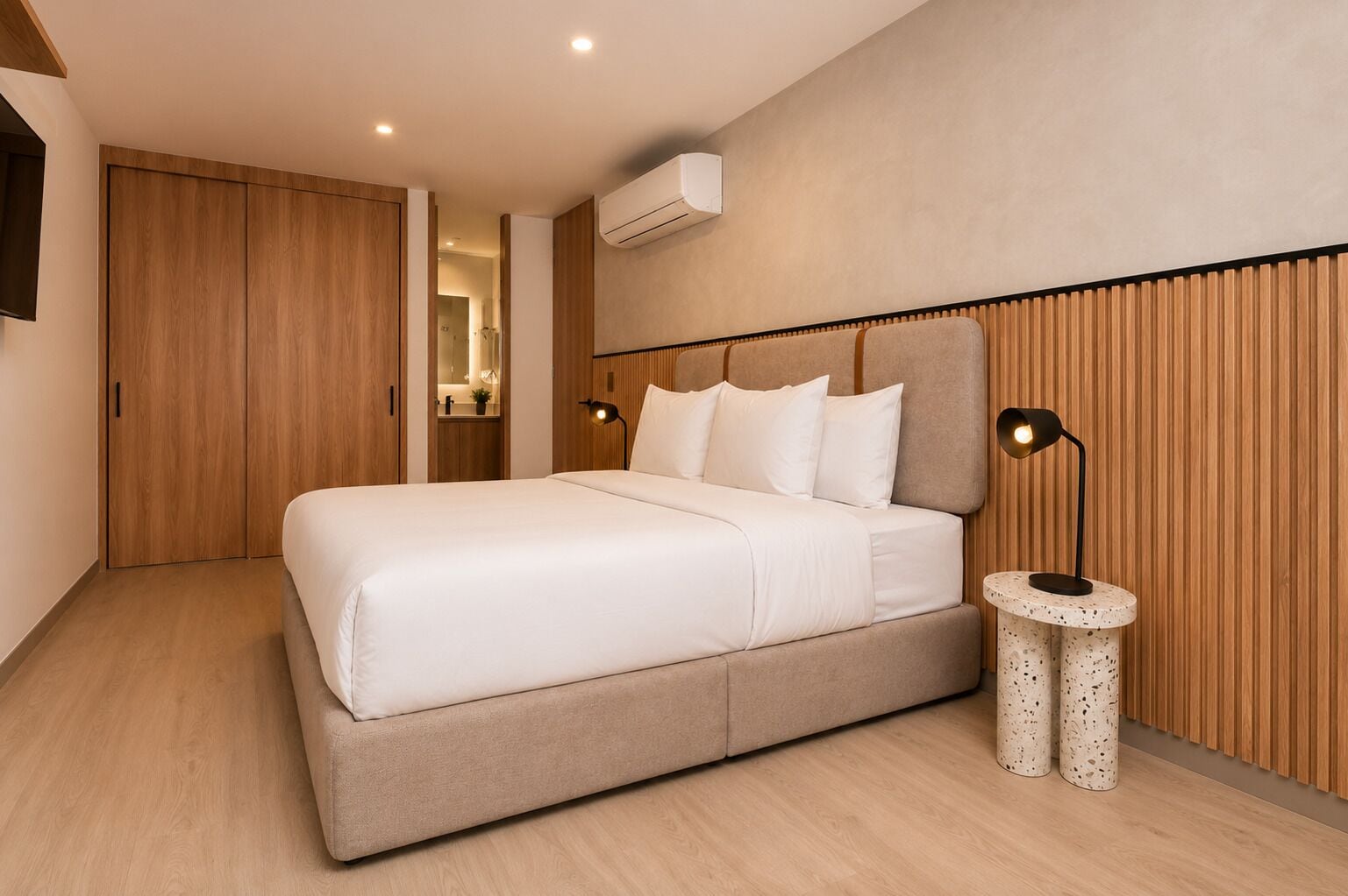 A modern bedroom with a large bed, wooden paneling, a wall-mounted air conditioner, and two bedside lamps.