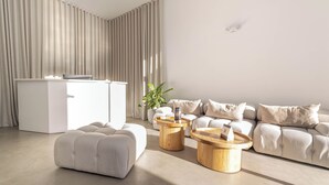 Een moderne woonkamer met een zithoek, twee houten salontafels, een wit bureau en een potplant.
