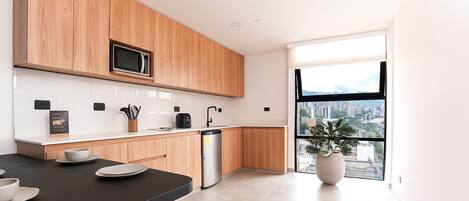 Una cocina moderna con armarios de madera, microondas, lavavajillas y un amplio ventanal con vistas a la ciudad.