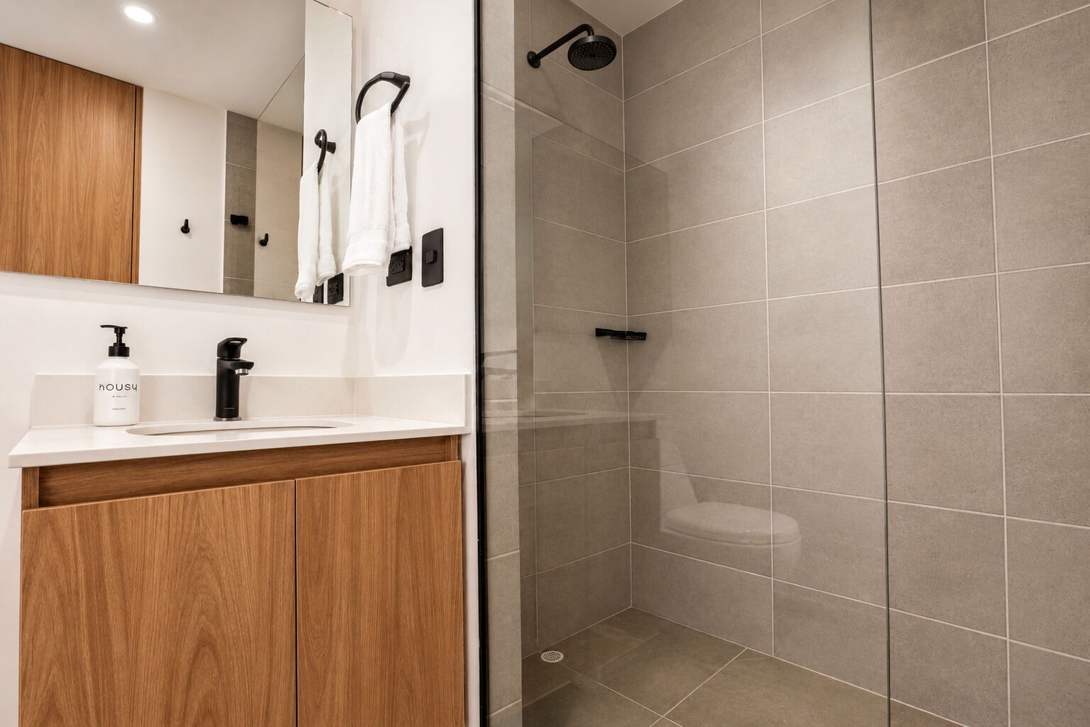 A modern bathroom with a wooden vanity, a white sink, and a glass-enclosed shower area.
