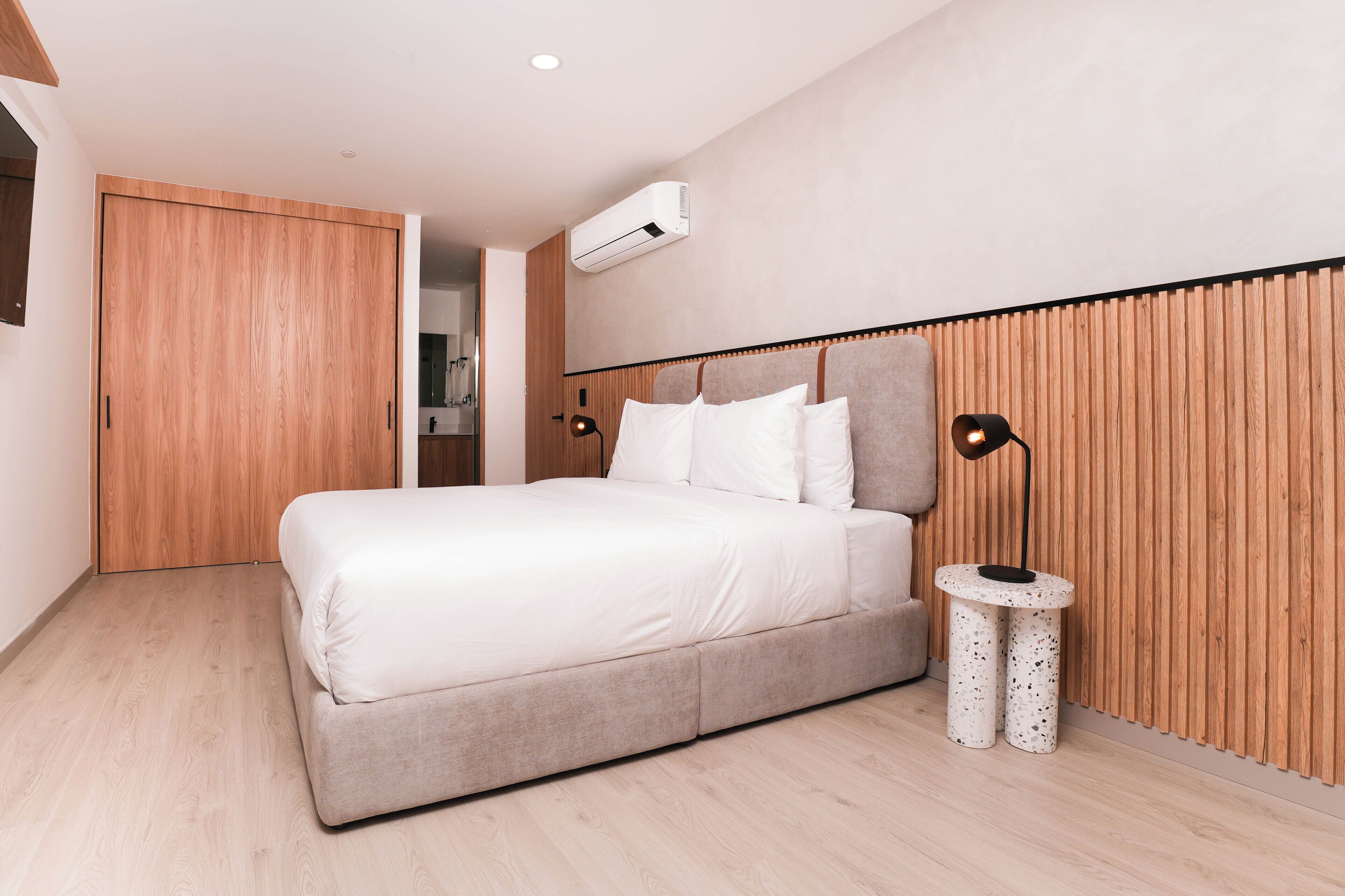 A modern bedroom with a large bed, wooden panel wall, and a small round table with a lamp.