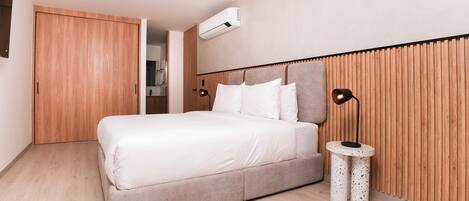 Un dormitorio moderno con una cama grande, un panel de pared de madera y una mesita redonda con una lámpara.