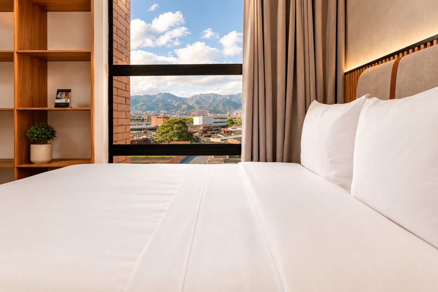 A hotel room with a large bed, a view of mountains, and a cityscape.
