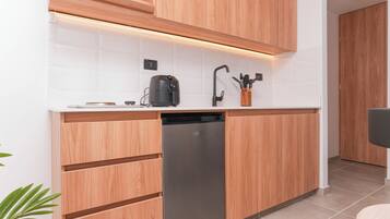 A compact kitchen with wooden cabinets, a built-in dishwasher, a coffee maker, and a knife holder.