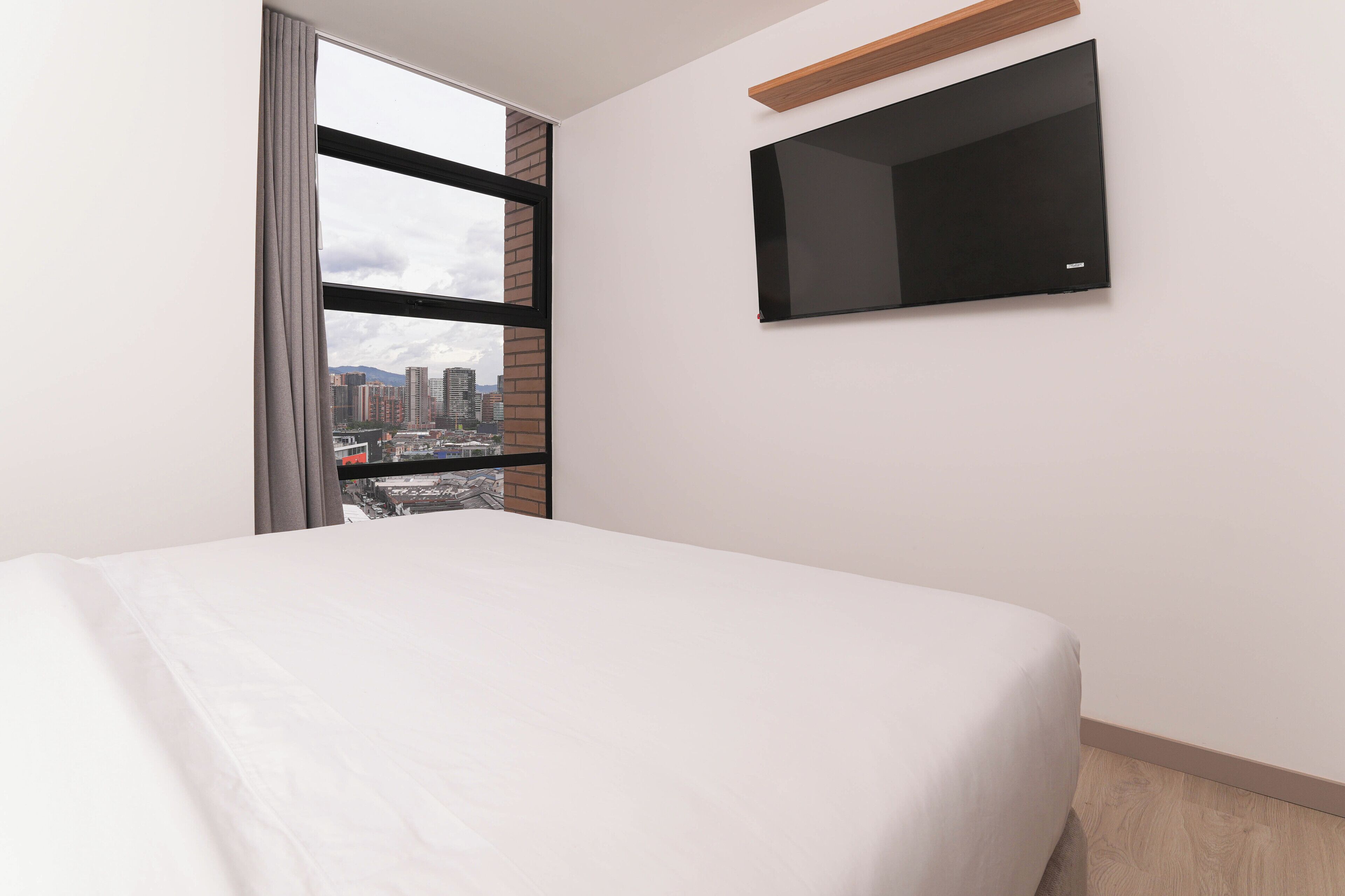 Een hotelkamer met een bed, een aan de muur bevestigde televisie en een raam met uitzicht op de stad.