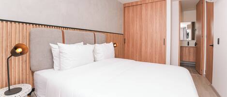 A modern bedroom with a large bed, wooden headboard, and a round nightstand with a lamp.