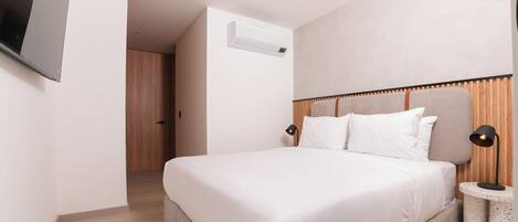 Una habitación de hotel moderna con una cama grande, un televisor de pantalla plana en la pared y una mesita de noche con una lámpara.