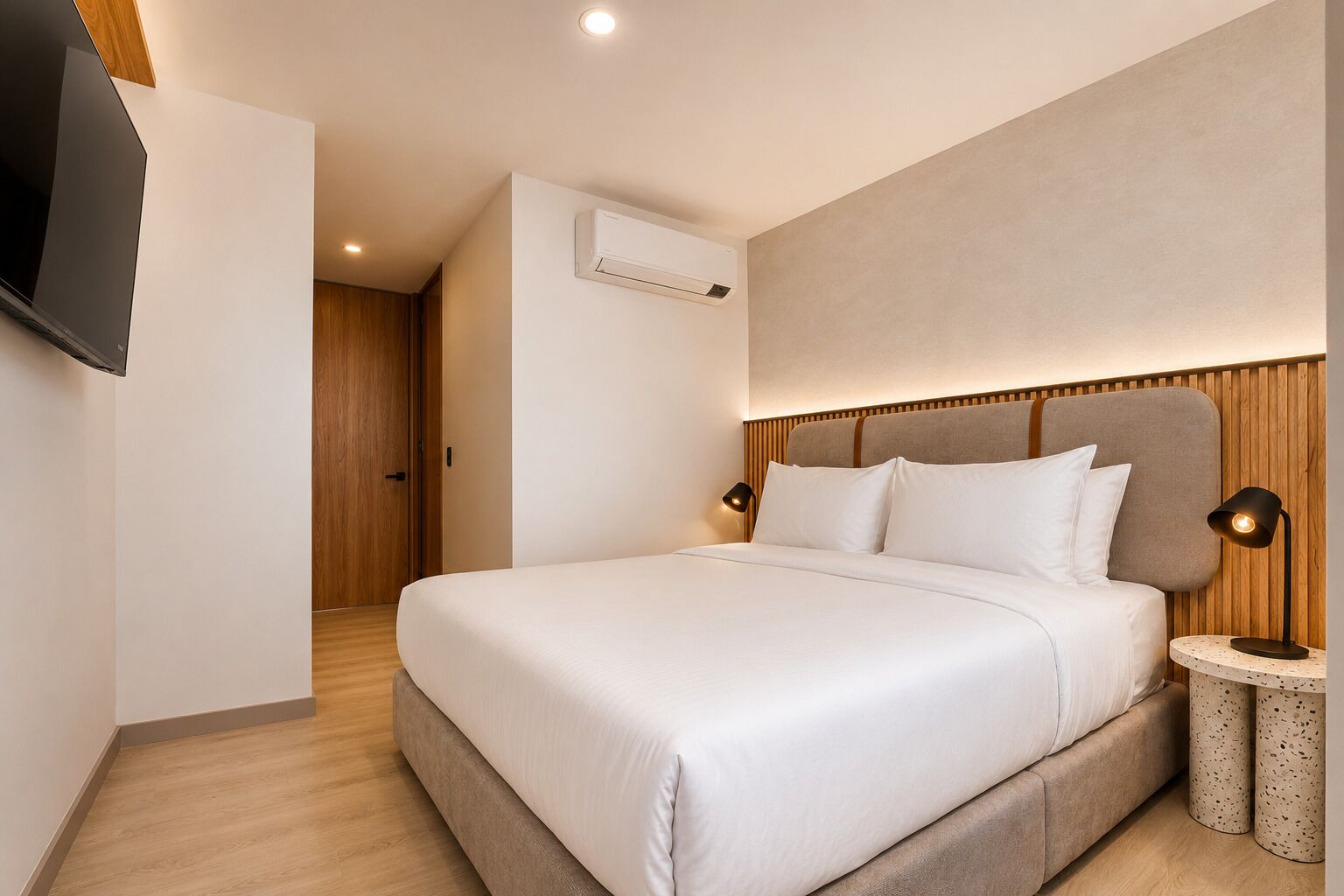Una habitación de hotel moderna con una cama grande, un televisor de pantalla plana en la pared, un equipo de aire acondicionado y un cabecero de madera.