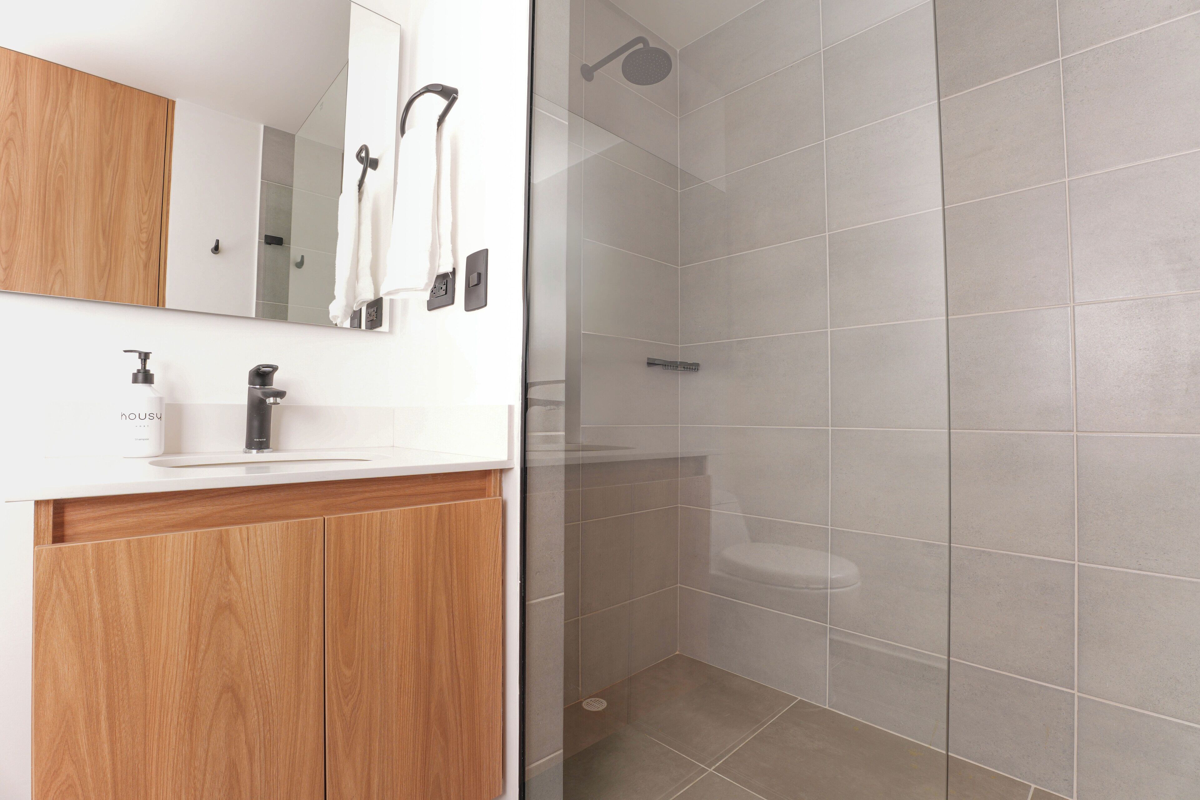 A modern bathroom with a wooden vanity, a mirror, a towel rack, and a shower area with tiled walls.