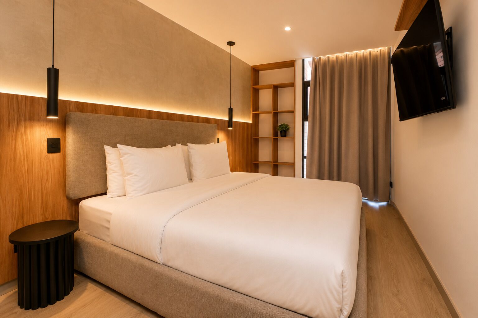 Una habitación de hotel moderna con una cama grande, mesitas de noche, un televisor y una estantería empotrada.