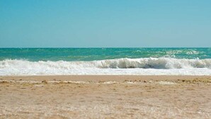 A beach with waves approaching the shore under a clear sky. - Sunrise and sunset sea views luxury 2Bedrooms apartments. (Ajman)