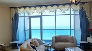 A living room with a sofa, armchair, and coffee table, large windows with curtains, and a chandelier. - Sunrise and sunset sea views luxury 2Bedrooms apartments. (Ajman)
