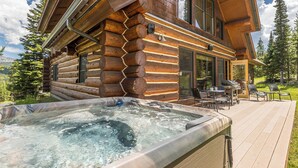 Een blokhut met een hottub op het terras, omringd door een dek en buitenmeubilair.