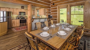 Een keuken in blokhutstijl met houten kasten, een roestvrijstalen koelkast en een eethoek met een houten tafel voor zes personen.