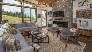 A modern living room with a stone fireplace, large windows, and a view of a green landscape.