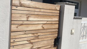 Una verja de madera con un tirador de metal que da a un edificio con un balcón y una ventana.
