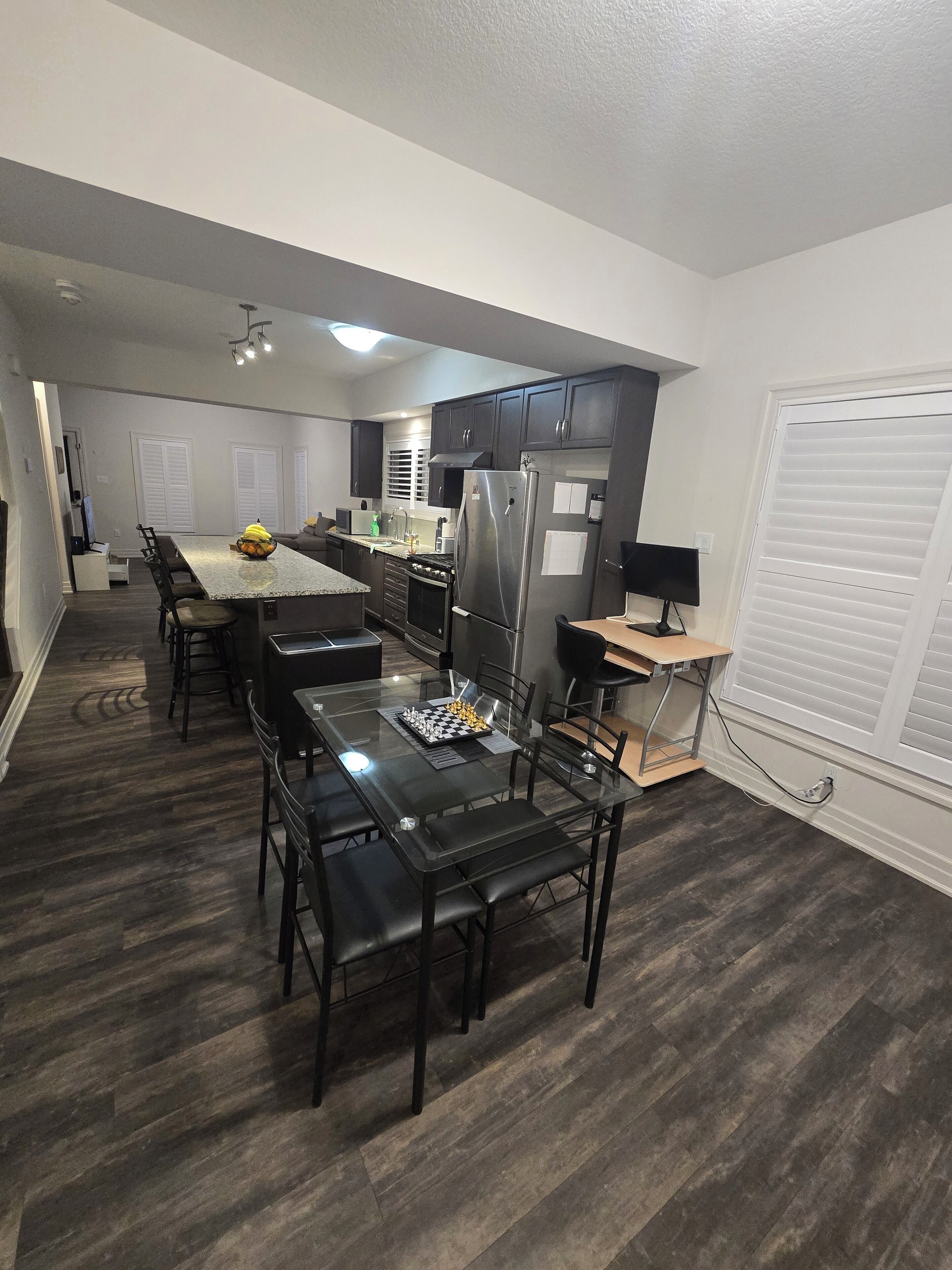 Cozinha moderna com piso de madeira escura, uma ilha central e uma área de refeições com cadeiras pretas.