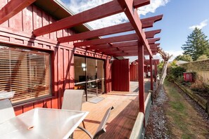 Eine überdachte Terrasse mit Tisch und Stühlen, ein Holzdeck und ein rotes Gebäudegerüst.