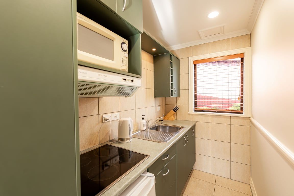 A compact kitchen with a microwave, kettle, and sink.