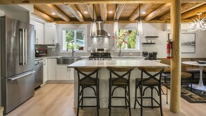 Une cuisine moderne dotée d’un grand îlot central, d’appareils électroménagers en acier inoxydable et de poutres en bois au plafond.