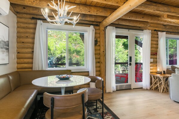 A cozy log cabin interior with a round dining table, leather seating, and a chandelier.