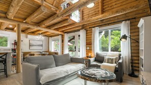 L’intérieur d’un chalet confortable, avec un canapé gris, une table basse ronde et un coin repas comprenant une table et des chaises en bois.