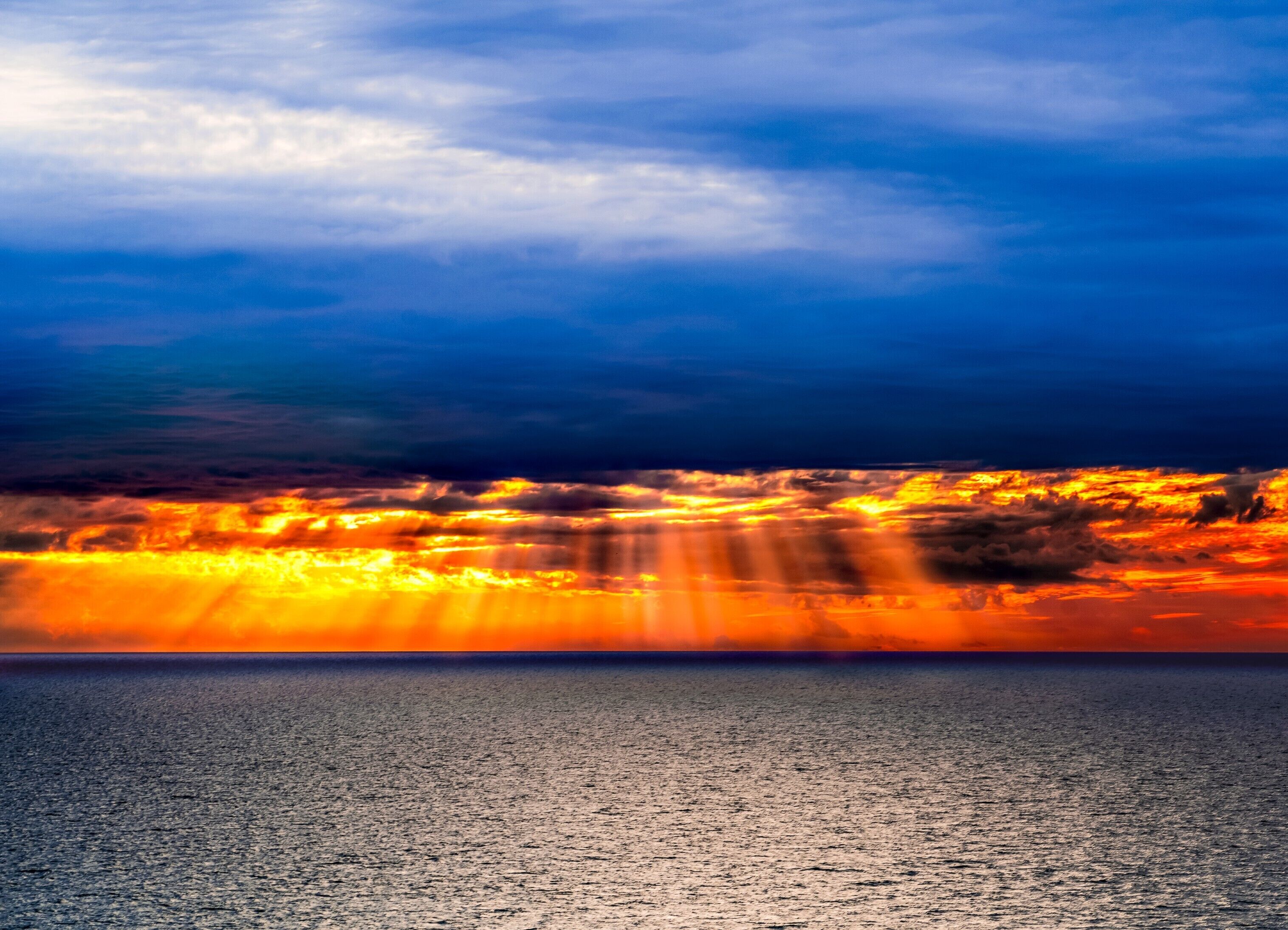 A sunset over a calm sea with a clear sky.