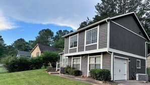 A two-story residential building with a dark siding exterior, a front garage door, and a well-maintained lawn. - Retreat at Stone Mountain – Cozy 3BR Near Trails, MARTA & Downtown (Stone Mountain)