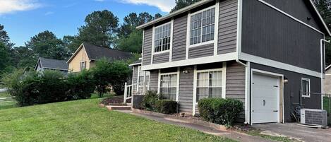 A two-story residential building with a dark siding exterior, a front garage door, and a well-maintained lawn.