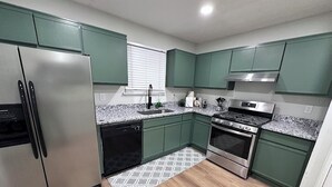 A modern kitchen with green cabinets, stainless steel appliances, a granite countertop, and a patterned rug. - Retreat at Stone Mountain – Cozy 3BR Near Trails, MARTA & Downtown (Stone Mountain)