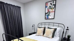 A neatly arranged bedroom with a metal-framed bed, white bedding, and a yellow throw. - Retreat at Stone Mountain – Cozy 3BR Near Trails, MARTA & Downtown (Stone Mountain)