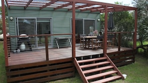 A wooden deck with a pergola structure, a dining table with chairs, and a grill.