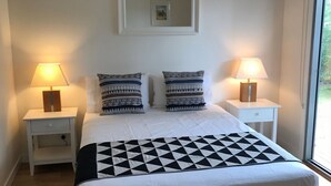 A neatly made bed with patterned pillows and a black and white geometric throw, flanked by bedside tables with lamps, in a room with a large window.