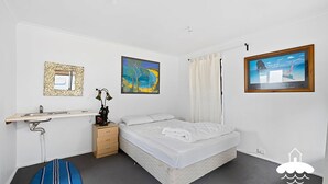A bedroom with a bed, a desk with a sink, a small drawer unit, and two framed pictures on the wall. - 14 Sunshine Rise Sandy Point (Sandy Point)