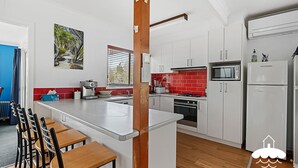 A modern kitchen with white cabinets, a red backsplash, and a central island. There is a painting on the wall, a window with blinds, and a microwave above the oven. - 14 Sunshine Rise Sandy Point (Sandy Point)