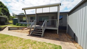 A covered outdoor area with a staircase leading to a deck, surrounded by a landscaped garden and a building with large windows. - 27 Beach Parade Sandy Point (Sandy Point)