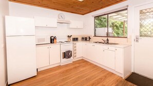 A compact kitchen with white cabinets, a microwave, stove, sink, and a window with a view of greenery.