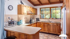 Een keuken met houten kastjes, een inbouwoven, een raam met uitzicht op groen, een klok aan de muur en een radio op het aanrecht.