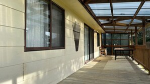 A covered porch with a wooden deck, large windows, and a metal roof structure.