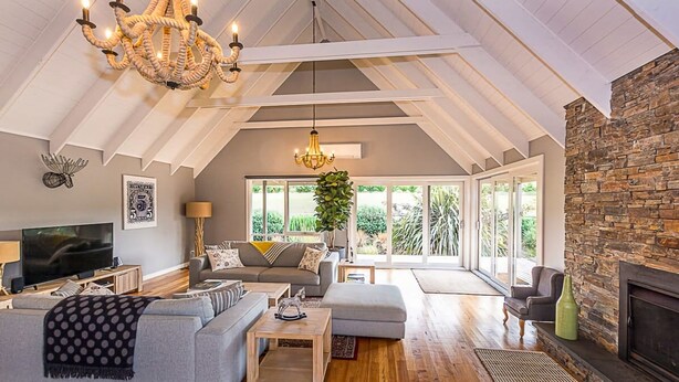 A spacious living room with a high ceiling, a fireplace, and large windows offering a view of the outdoors.