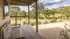 A wooden deck with a bench, overlooking a grassy field with trees and a tractor.
