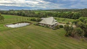 A large house with a pond, surrounded by lush green fields and trees.