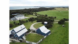 Una extensa granja con varias edificaciones, entre ellas una casa principal y graneros, rodeada de campos verdes y una masa de agua al fondo.