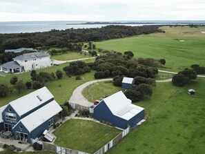 Una extensa granja con varias edificaciones, entre ellas una casa principal y graneros, rodeada de campos verdes y una masa de agua al fondo.