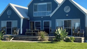 Una casa moderna de dos pisos con fachada azul, ventanas amplias y un porche delantero con mobiliario exterior.