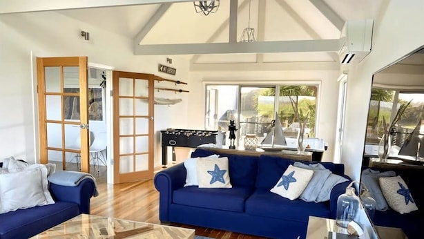 Amplia sala de estar con un sofá azul, una mesa de centro de cristal y piso de madera.