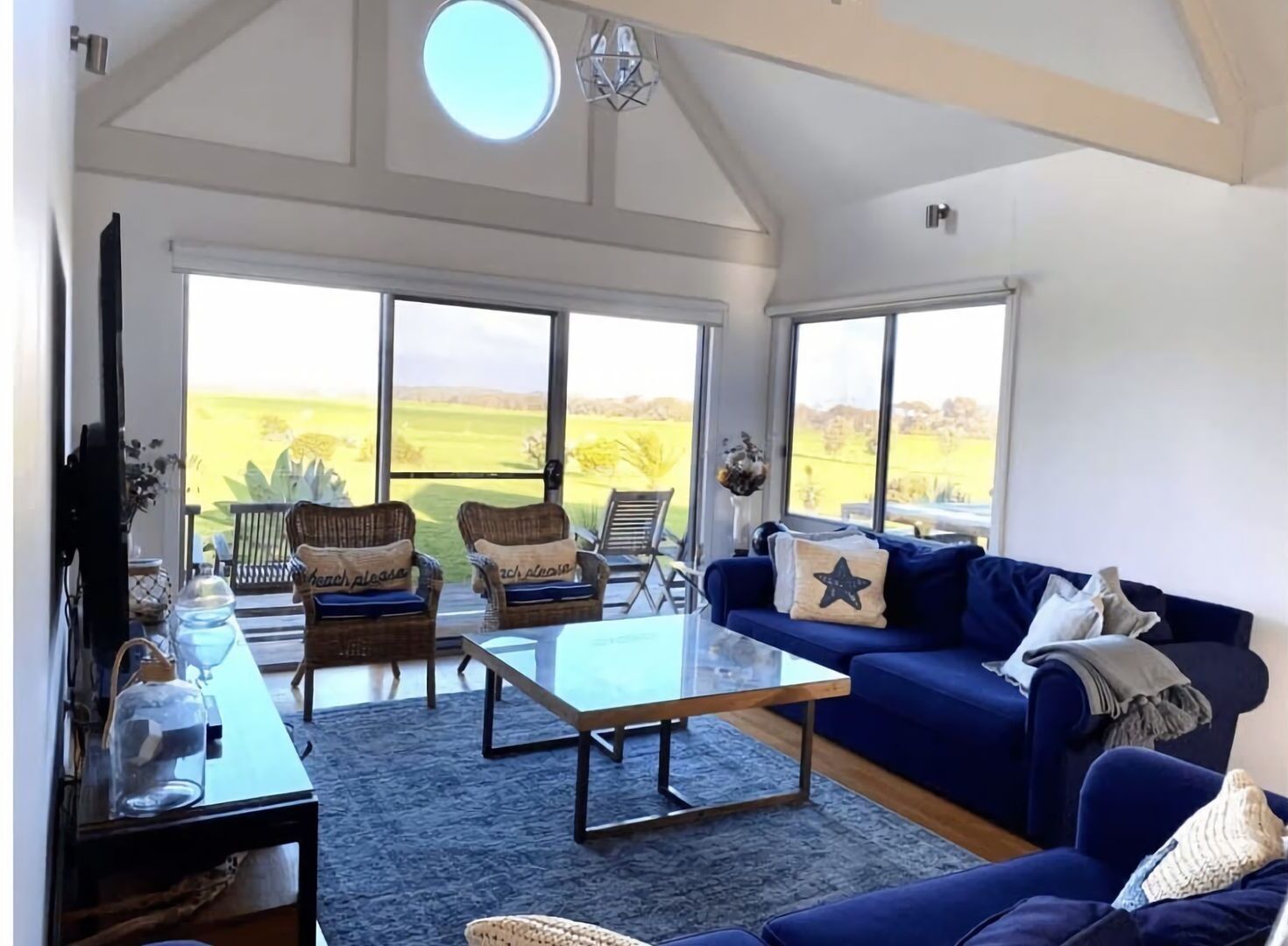 A spacious living room with a large window, a blue sofa, wicker chairs, and a coffee table.