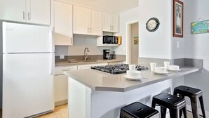 A modern kitchen with white cabinets, a built-in microwave, a gas stove, and a small island with bar stools.
