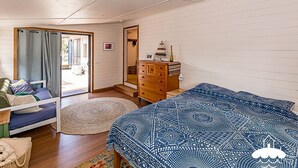 A bedroom with a bed, a dresser, a chair, and a door leading to an outdoor area.